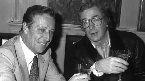 PA Media Frederick Forsyth and Michael Caine drinking together in 1986