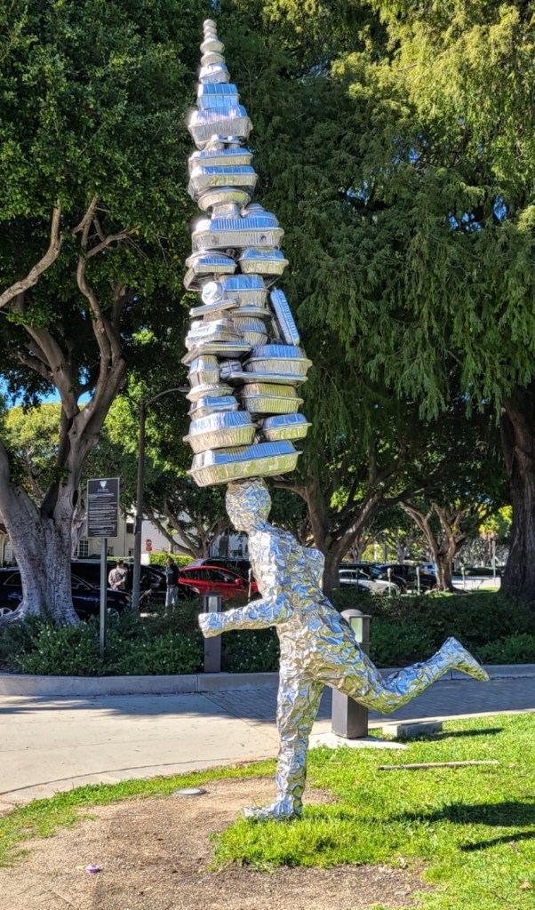 “Takeaway,” 2018, Tom Friedman. Public art shows silver man balancing numerous takeaway boxes on his head.